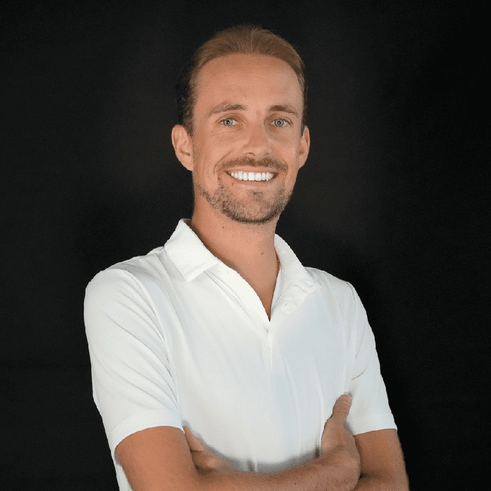 photo displaying a man wearing a white polo smiling into the camera