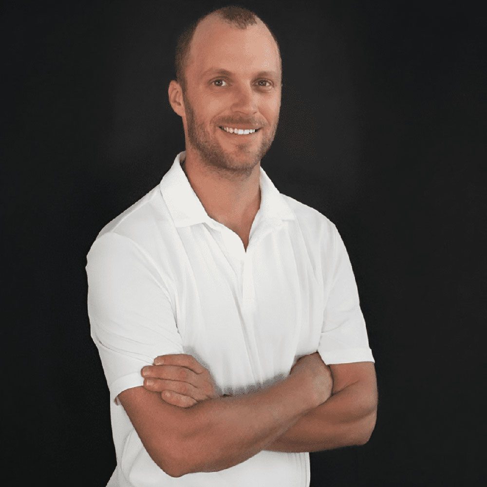 photo displaying a man wearing a white polo smiling into the camera