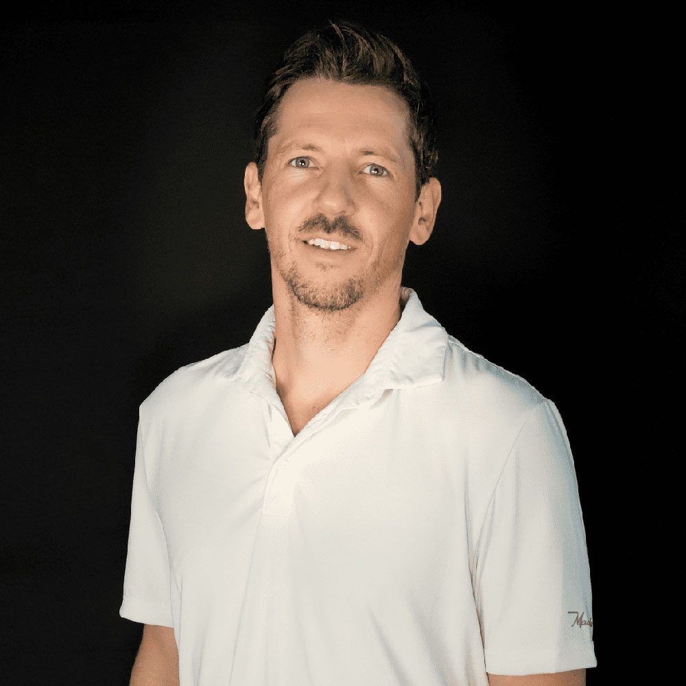 photo displaying a man wearing a white polo smiling into the camera