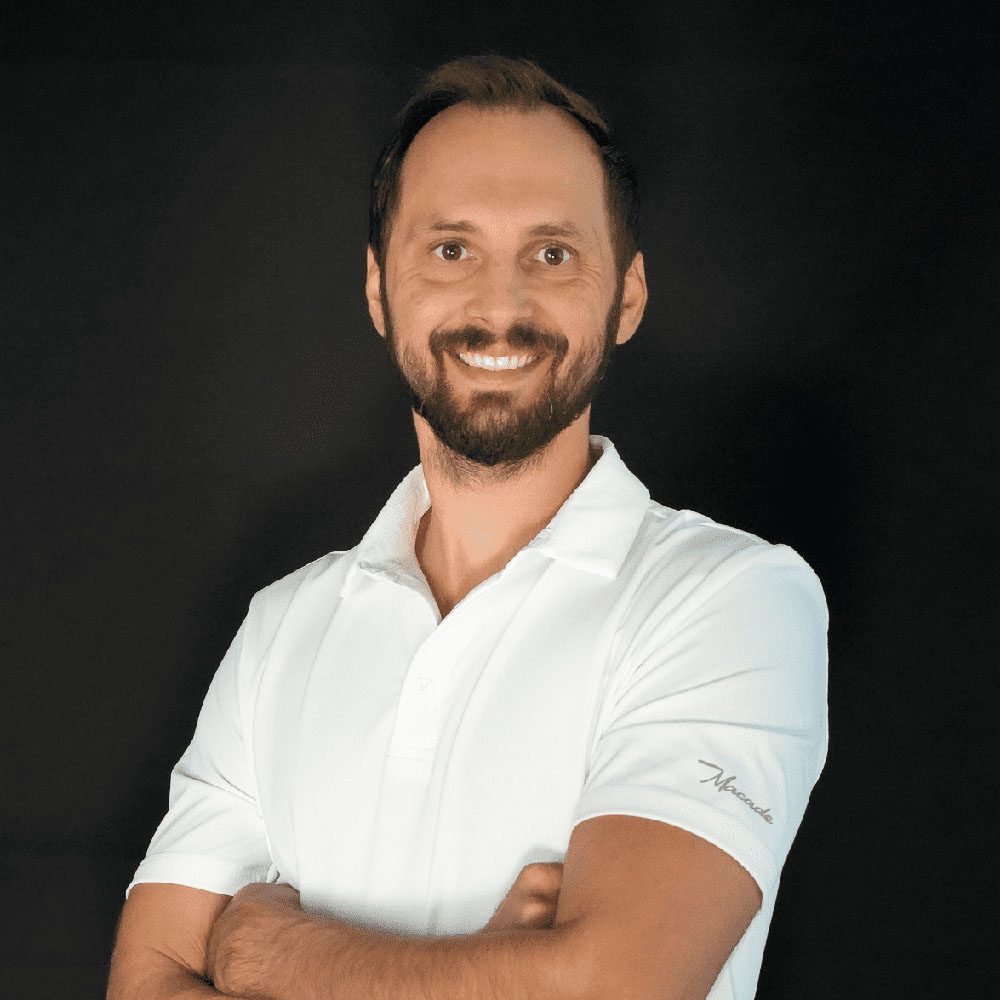 photo displaying a man wearing a white polo smiling into the camera